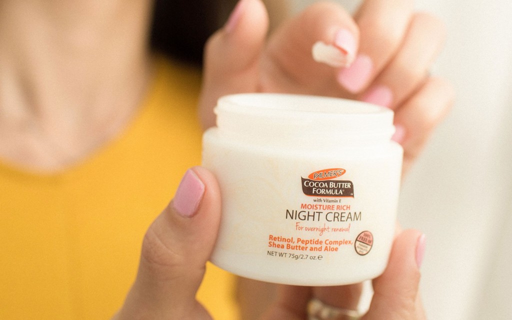 Palmer's Cocoa Butter Formula Night Renewal Cream, an essential in the best nighttime skin care routines, in hand with cream on finger